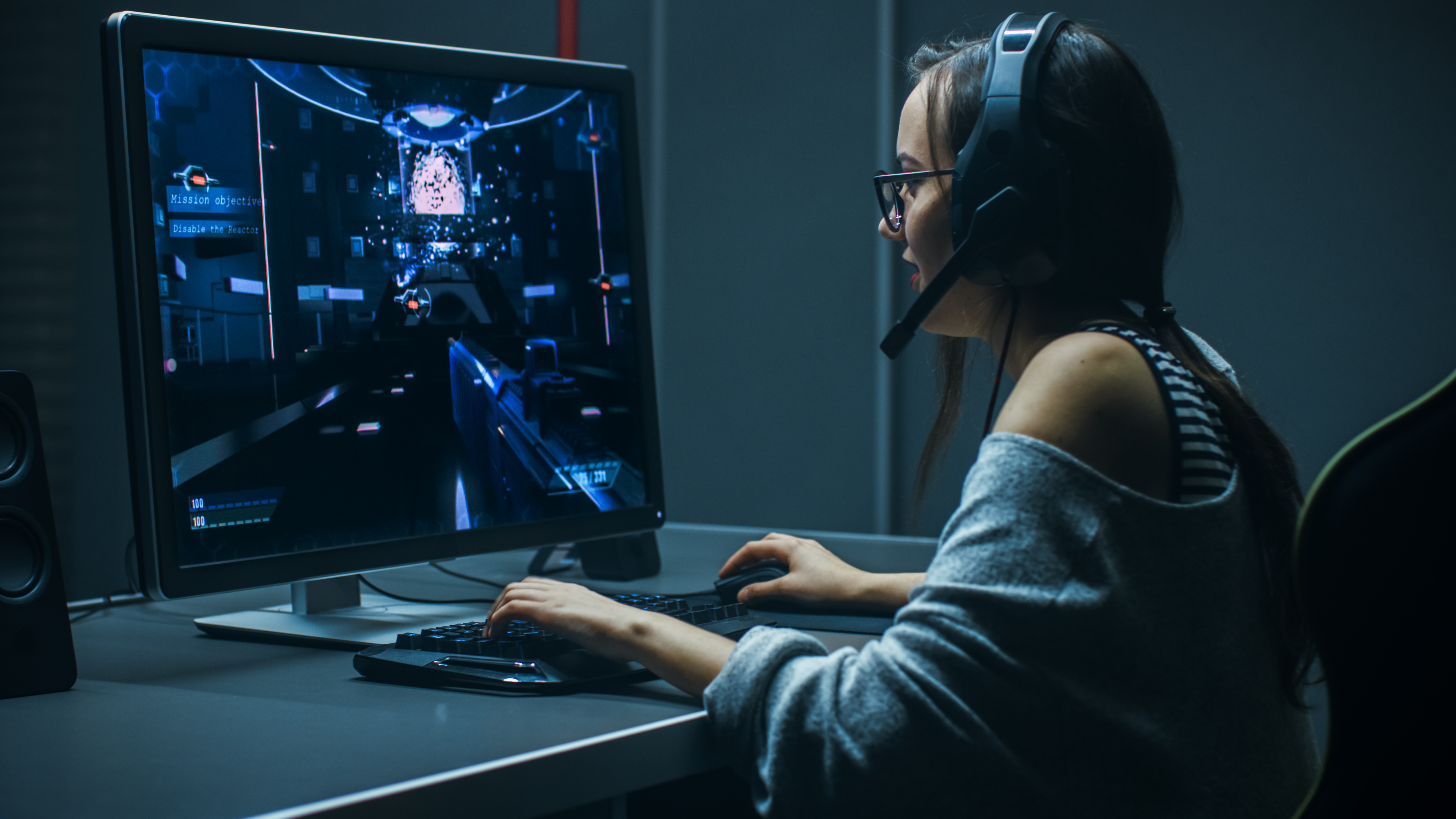 Female gamer playing on a large computer monitor with keyboard, mouse and her headset on.