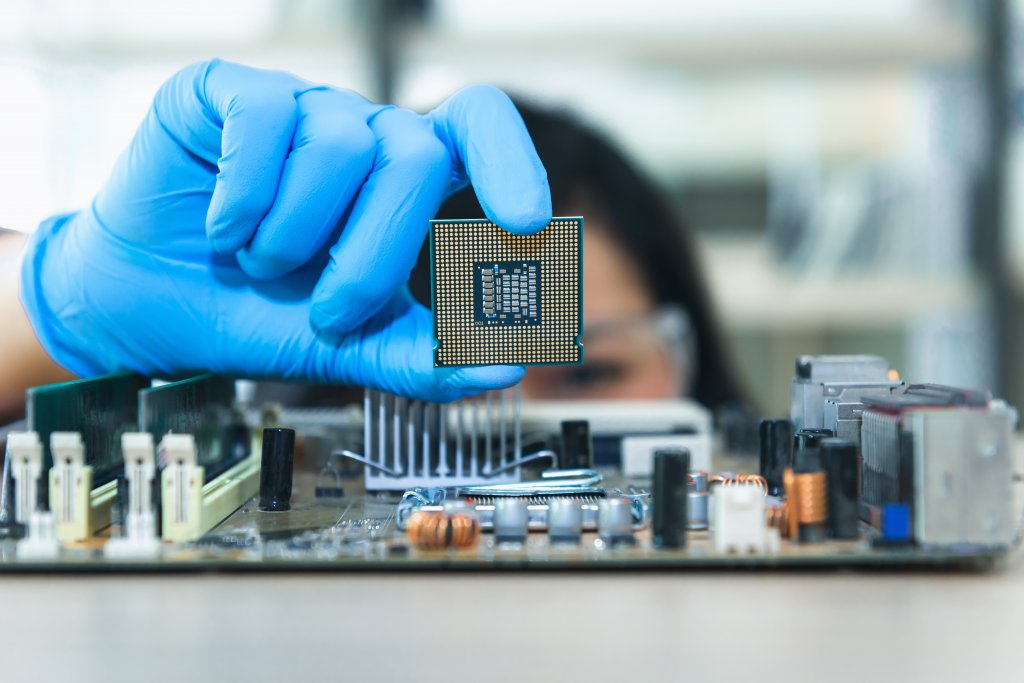 Close up portrait of a female computer engineer's hand holding up a CPU above a motherboard